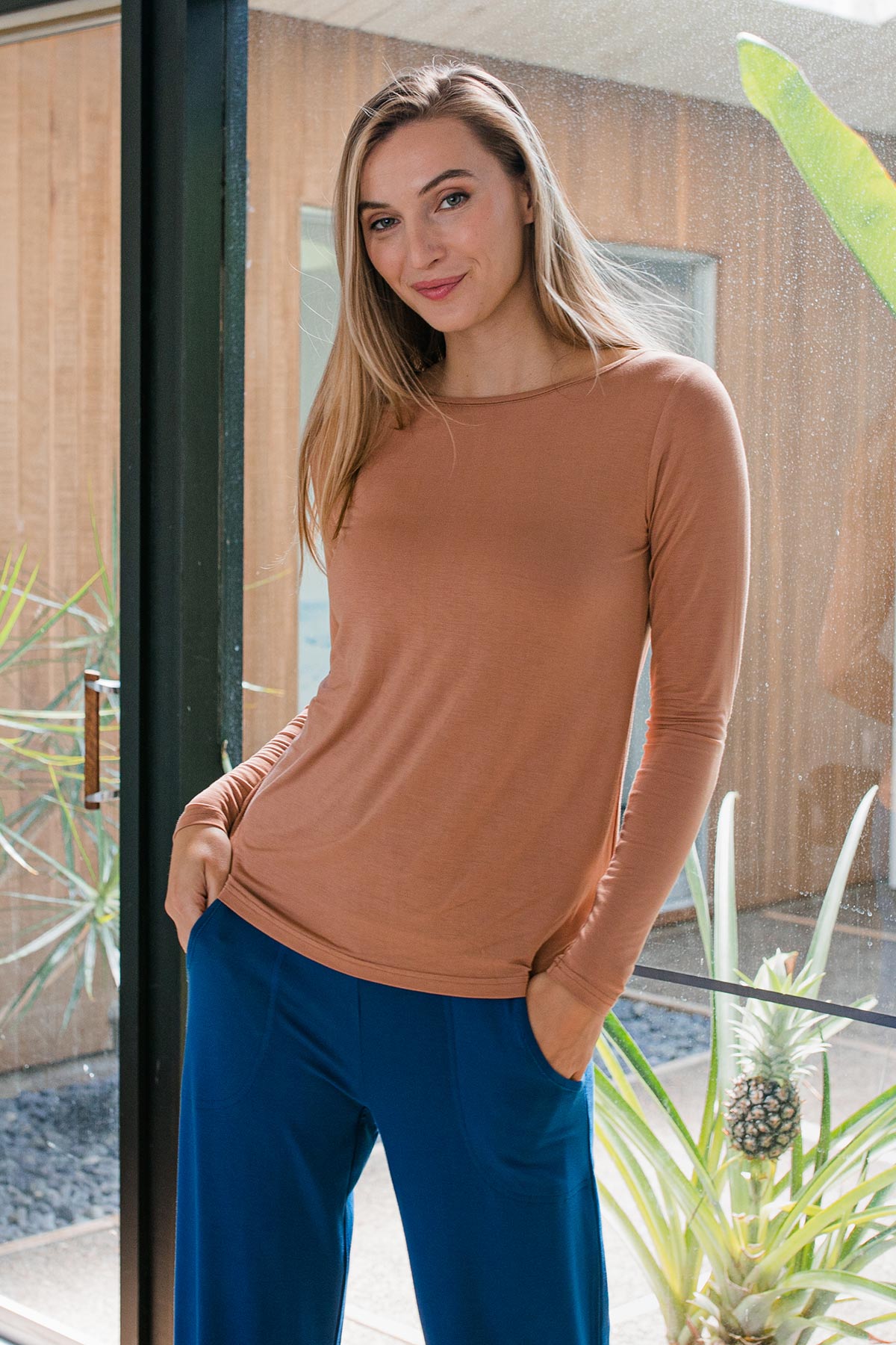 A woman standing and smiling with her hands in her pockets, wearing Yala Jena Long Sleeve Bamboo Tee Shirt in Camel