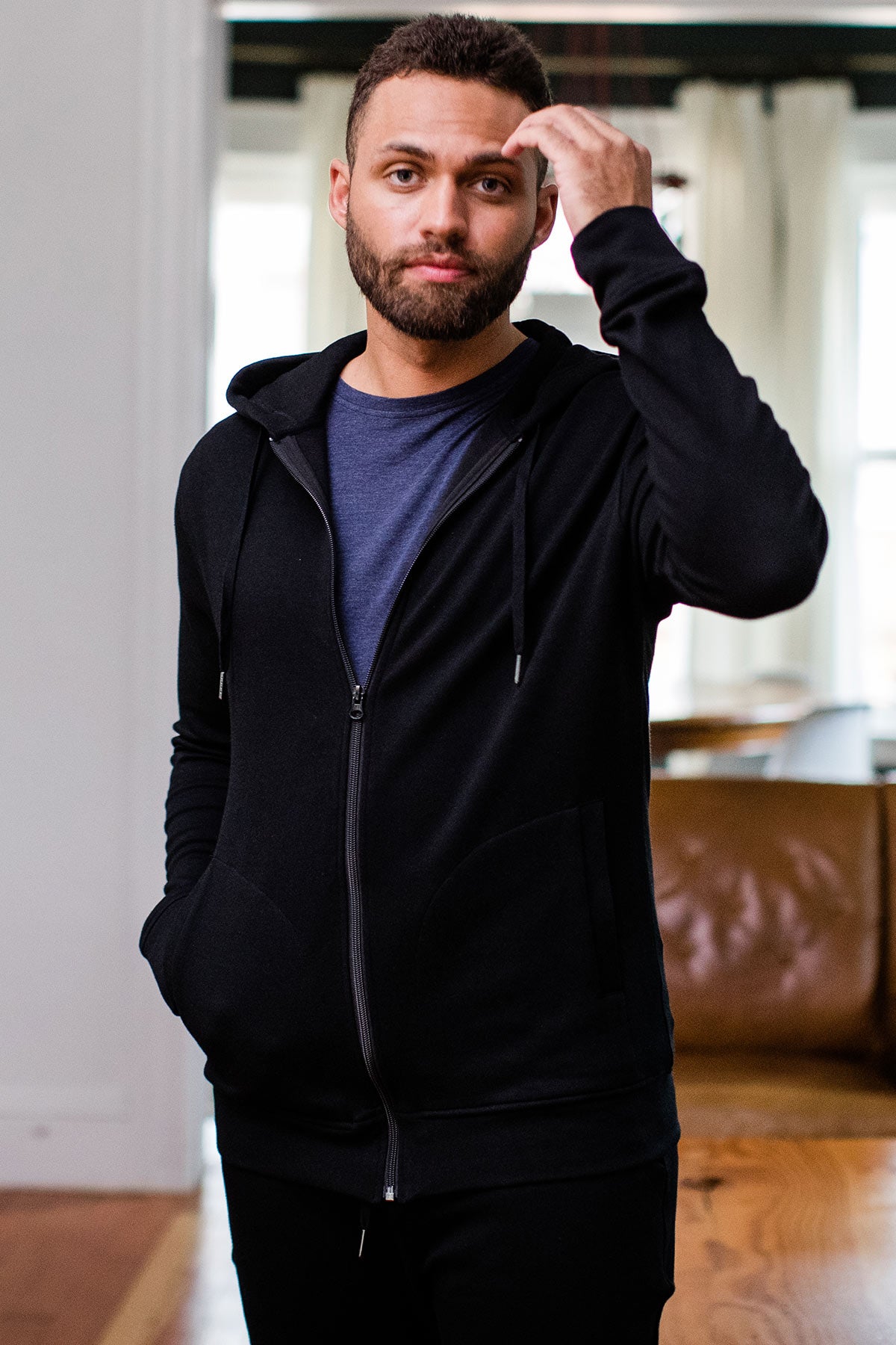 A man standing with one hand in his pocket and the other raised to his head, wearing Yala Joey Men's Zip-Up Bamboo and Organic Cotton Sweatshirt Hooded Jacket in Black