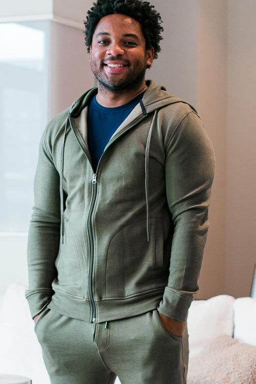 A man standing and smiling with both hands in his pockets, wearing Yala Joey Men's Zip-Up Bamboo and Organic Cotton Sweatshirt Hooded Jacket in Moss