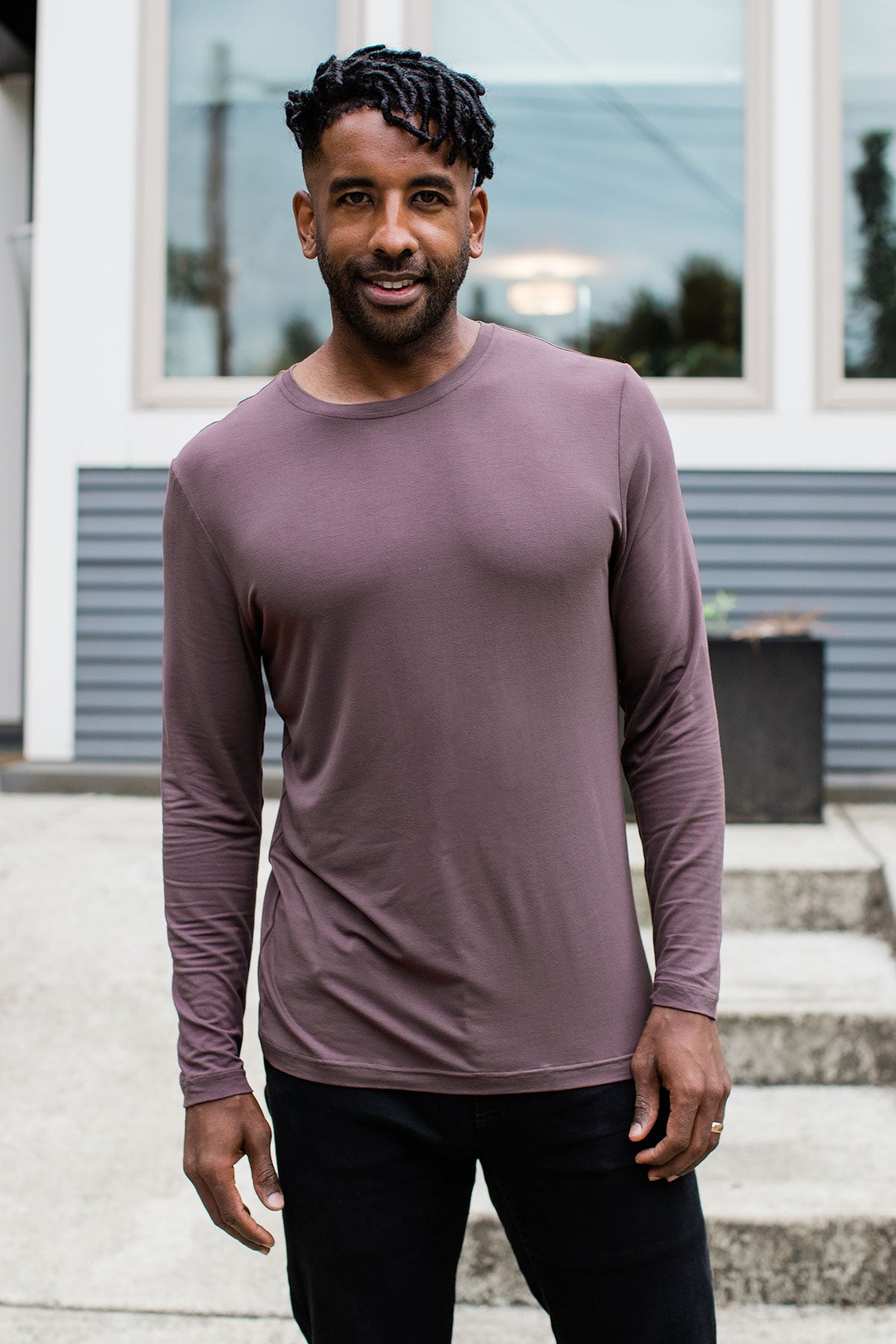 A man standing and smiling with both hands at his sides, wearing Yala Jonah Men's Long Sleeve Bamboo Crew Tee Shirt in Mink