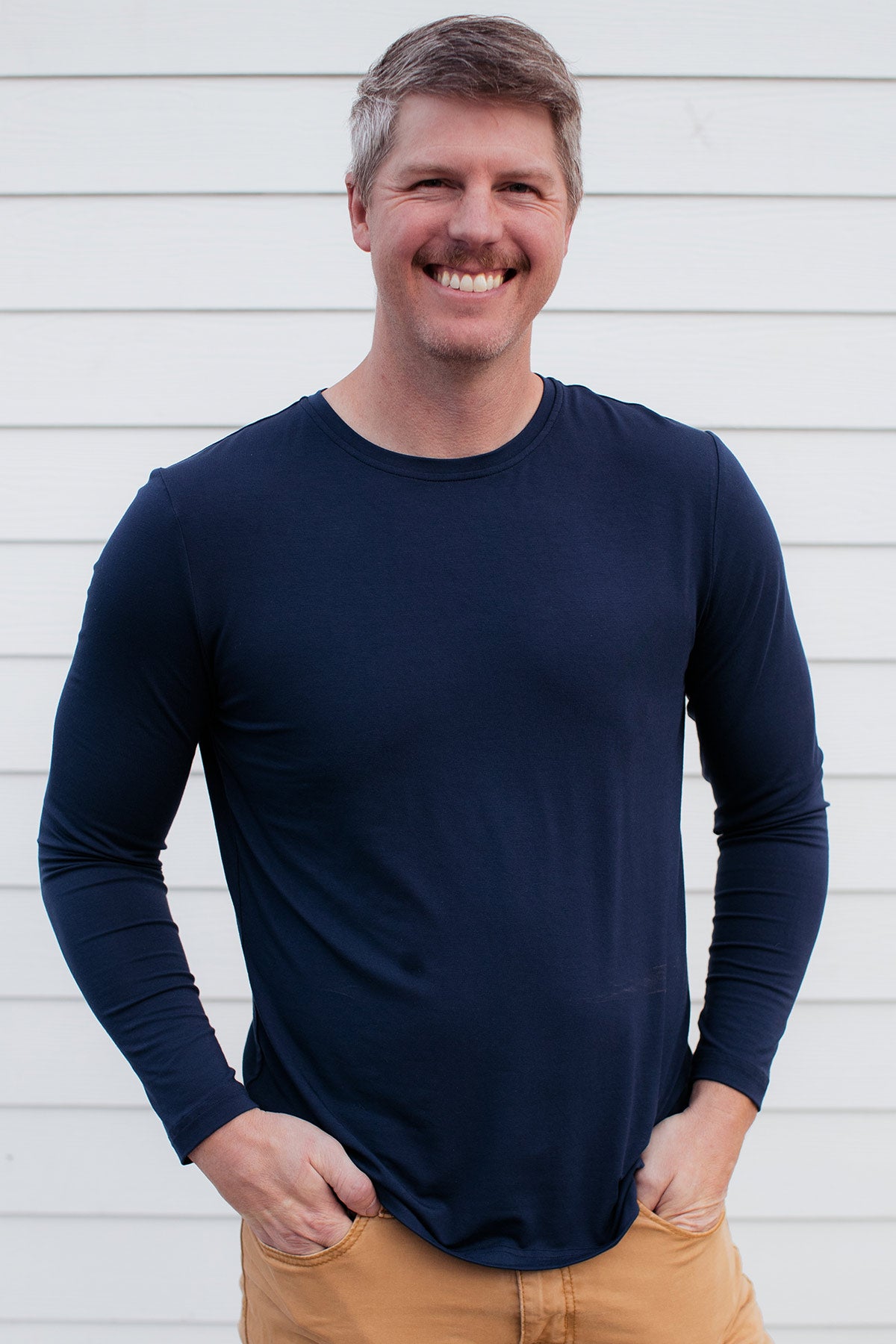A man standing and smiling with both hands in his pockets, wearing Yala Jonah Men's Long Sleeve Bamboo Crew Tee Shirt in Navy