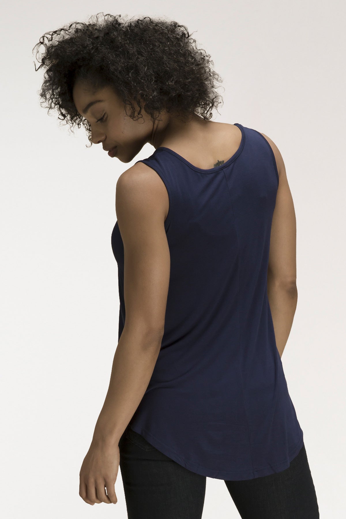 A woman standing with her back turned, looking back over her shoulder, wearing Yala Justine Bamboo Tunic Tank Top in Navy