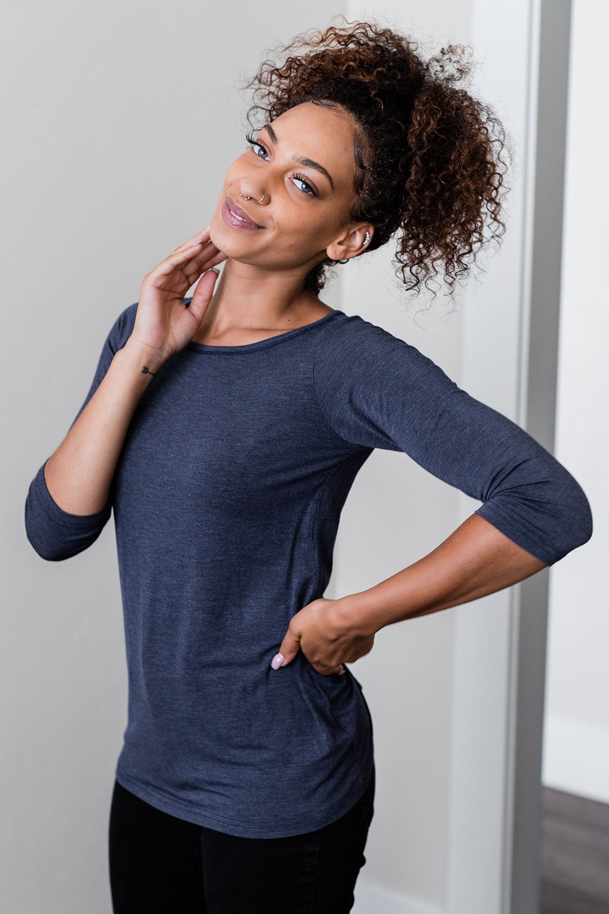 A woman standing with one hand on her hip and one hand on her chin, wearing Yala Kai Boatneck Three Quarter Sleeve Relaxed Fit Bamboo Tee Shirt in Navy Melange