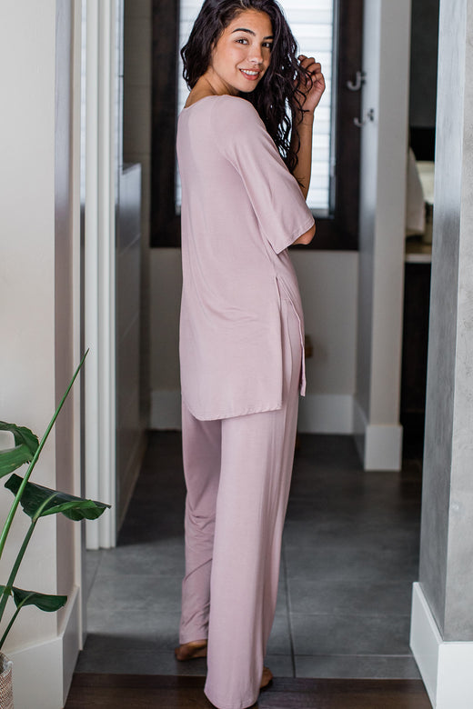 A woman standing facing away from the camera while looking back over her shoulder, wearing Yala Kat Lounge Bamboo Pajama Set in Lotus Pink