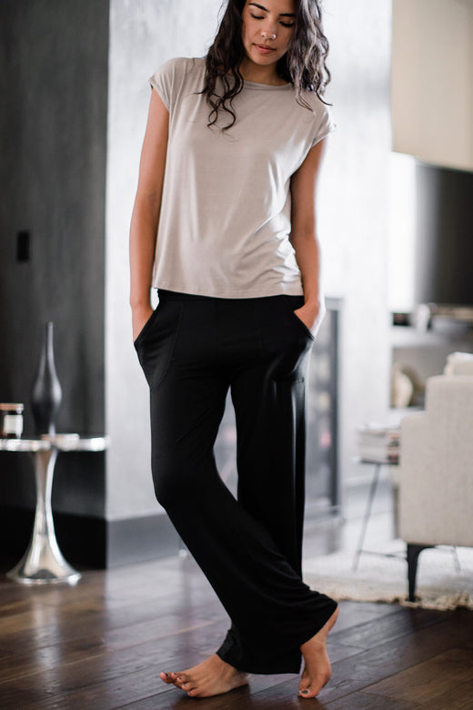 A woman standing with one leg crossed in front of the other and both hands in her pockets, wearing Yala Kayla Wide Leg Foldover Waist Bamboo Pants in Black