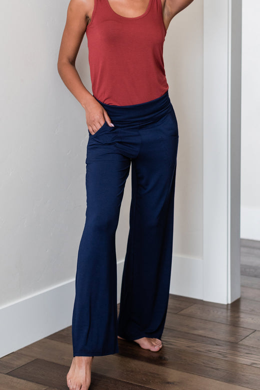 A headless shot of a woman with one foot forward and one hand in her pocket, wearing Yala Kayla Wide Leg Foldover Waist Bamboo Pants in Navy