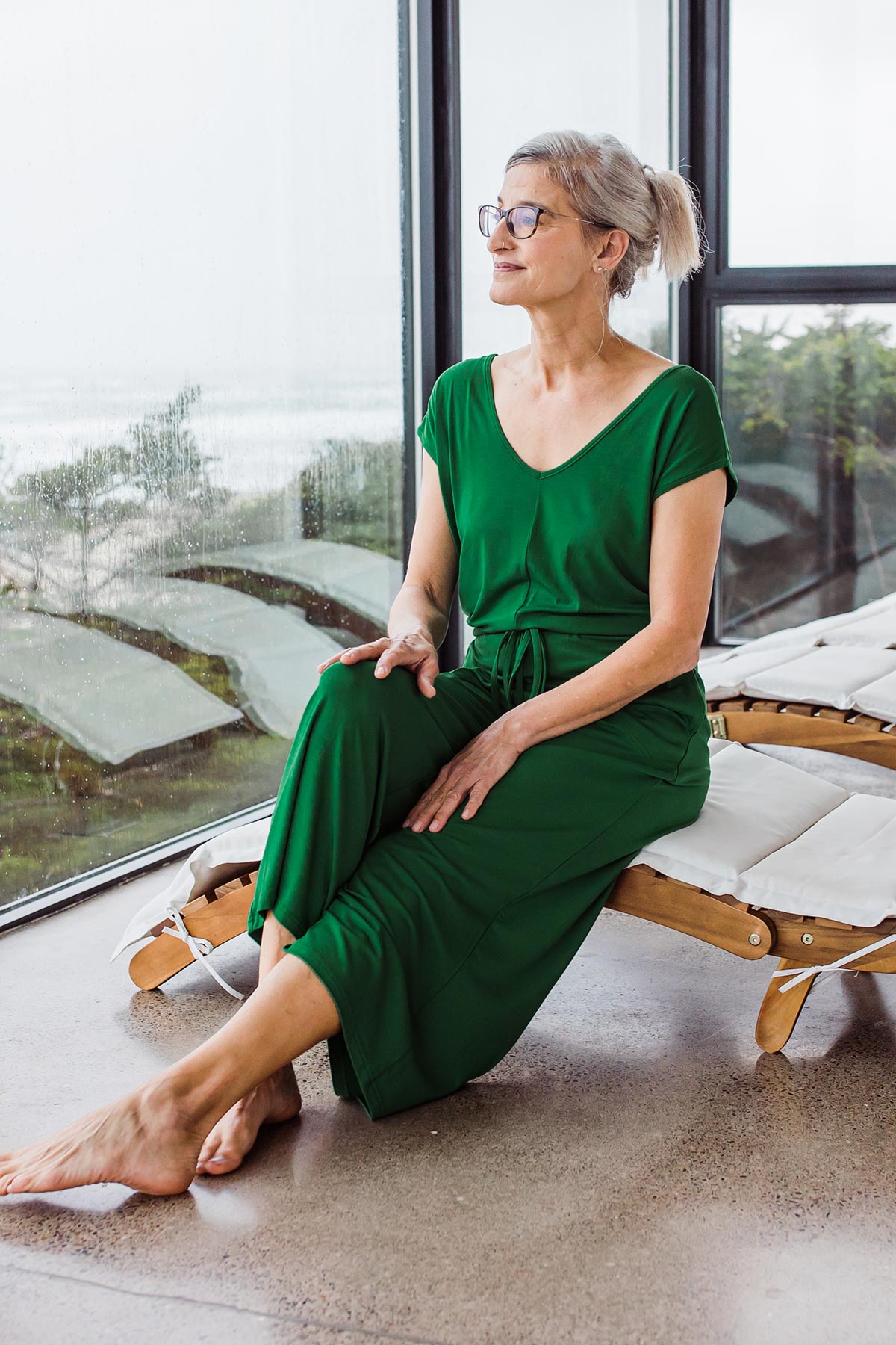 Woman sitting and looking out of a window, wearing Yala Kiova V-Neck Bamboo Jumpsuit in Emerald