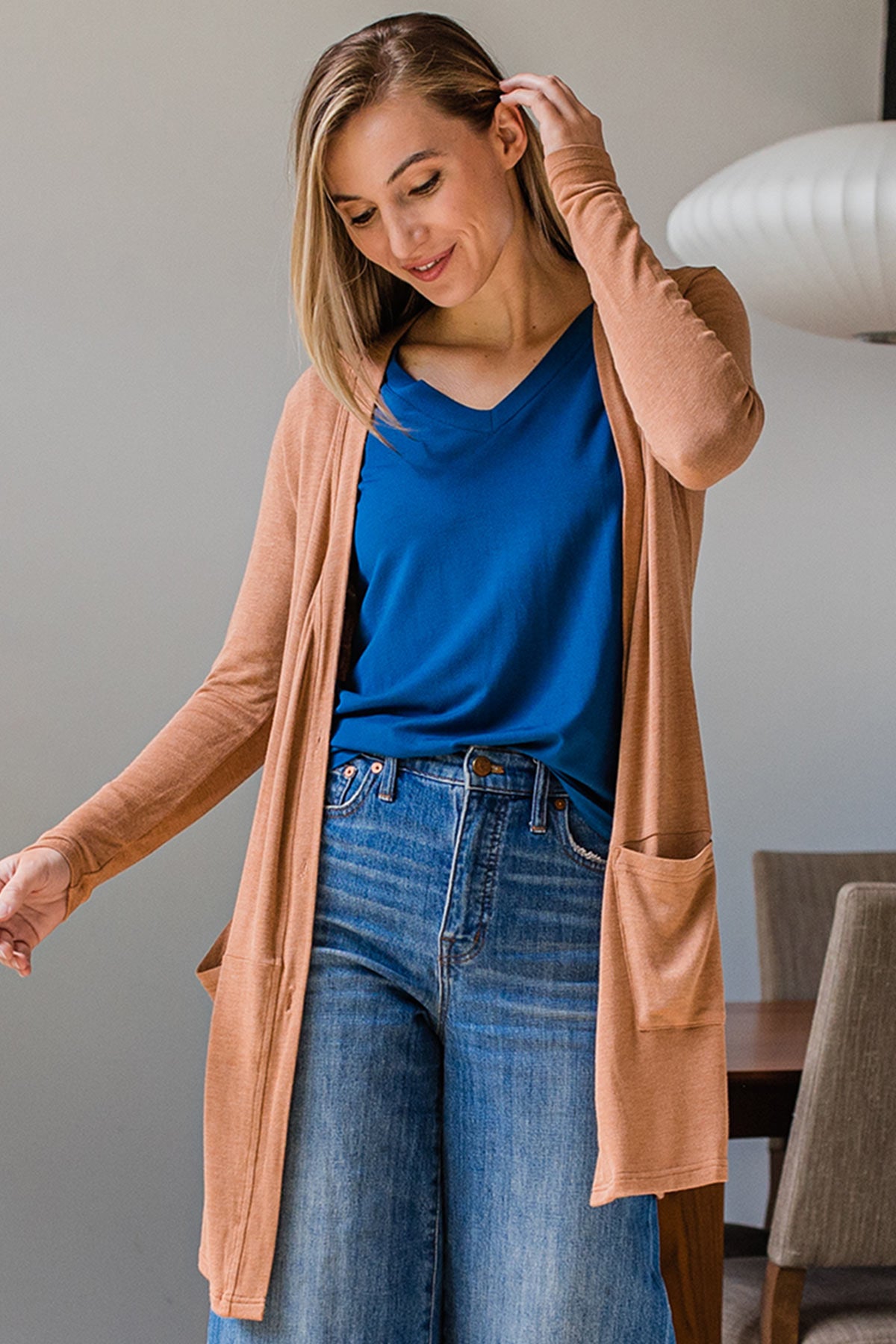 A woman standing and looking downward while brusing her hair aside with one hand, wearing Yala Leslie Long Sleeve Oversize Bamboo Cardigan in Camel