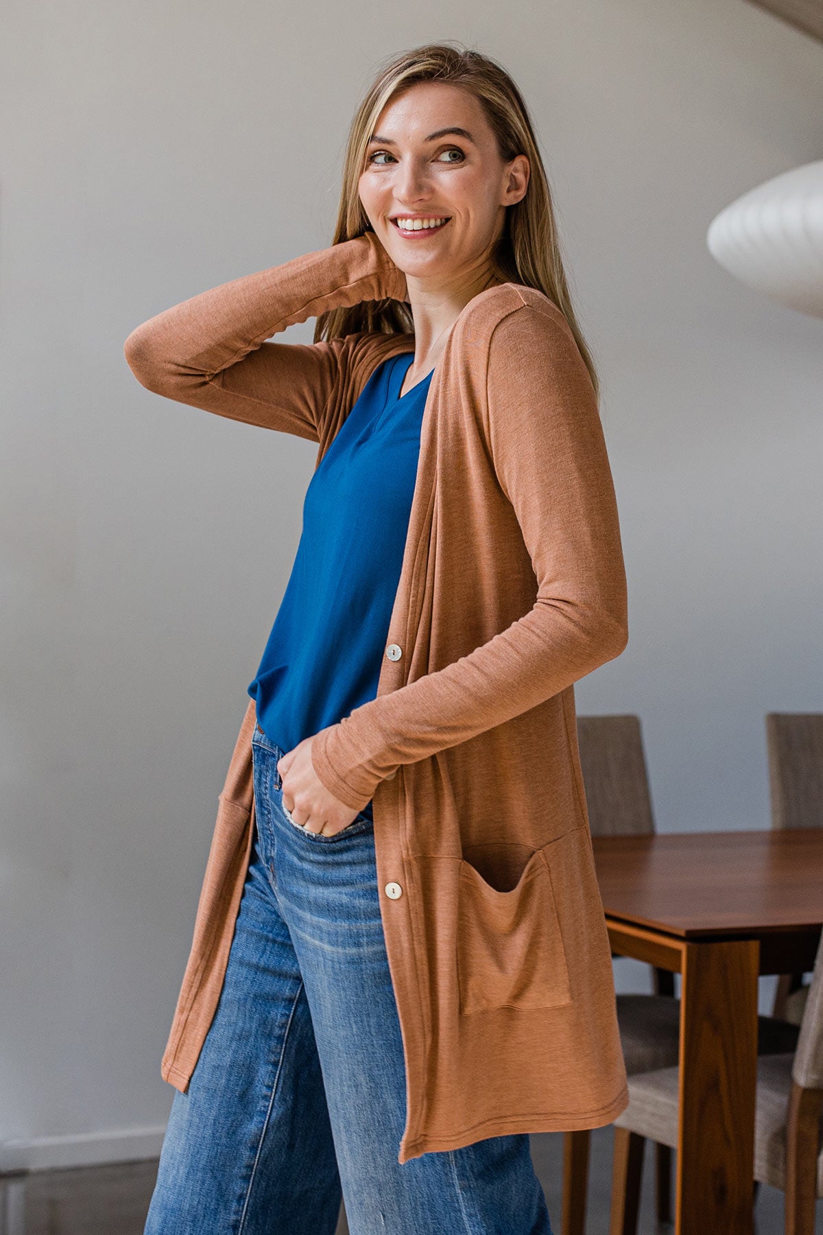 A woman standing sideways with one hand on her neck, looking towards the camera, wearing Yala Leslie Long Sleeve Oversize Bamboo Cardigan in Camel
