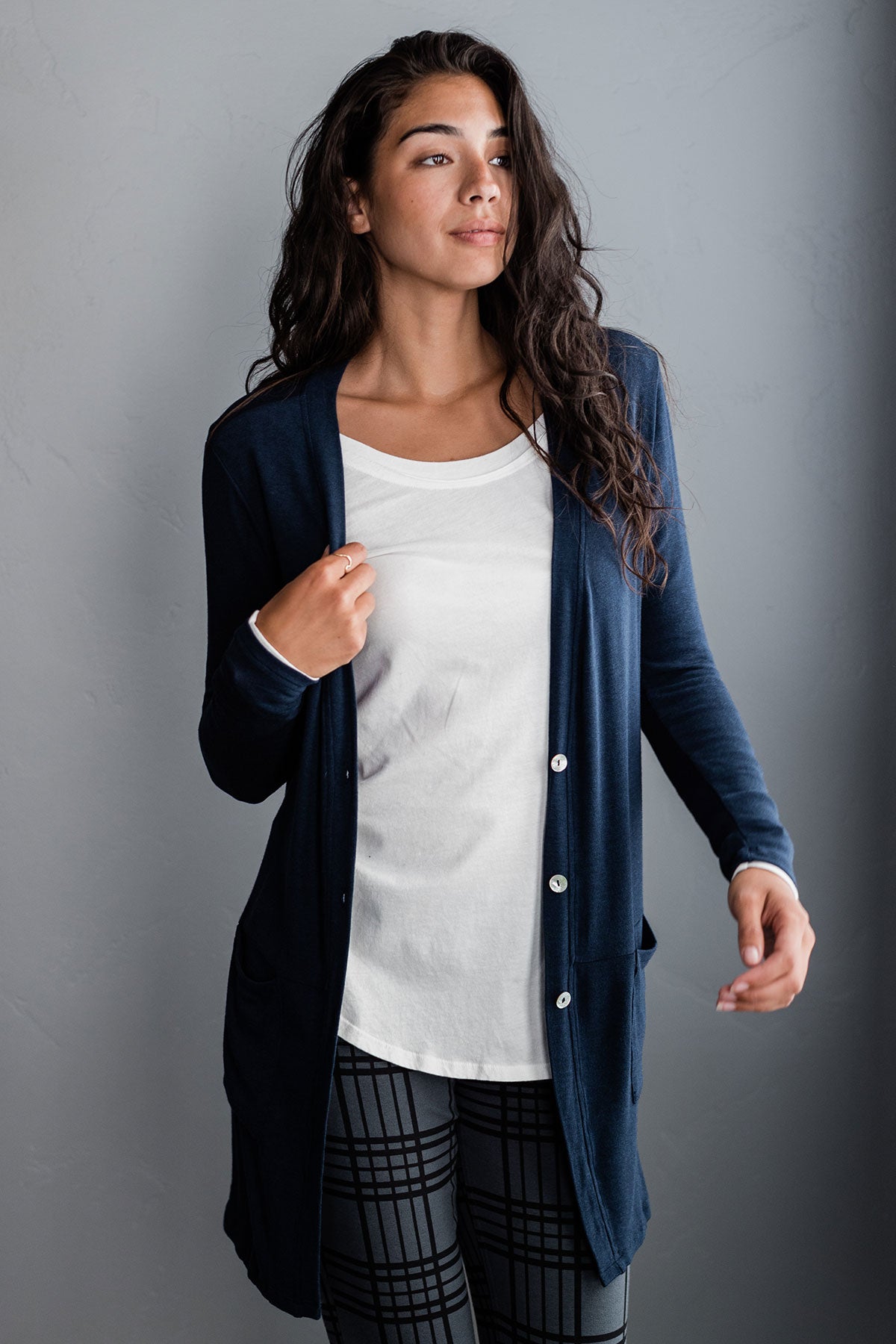 A woman standing and looking off to the side, wearing Yala Leslie Long Sleeve Oversize Bamboo Cardigan in Navy