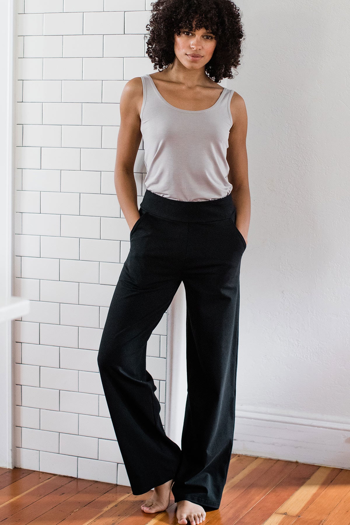 A woman standing and leaning against a wall with one knee bent, wearing Yala Lexi Ultra-Stretch Bamboo and Organic Cotton Classic Wide Leg Pants in Black