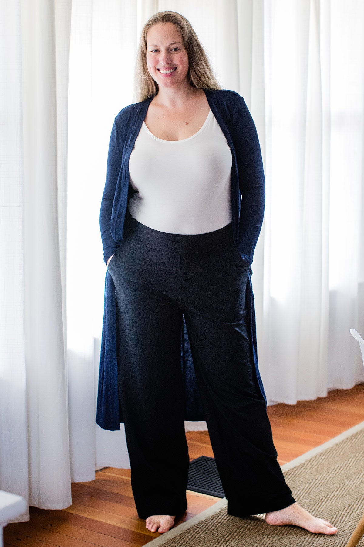 A woman standing and smiling with both hands in her pockets, wearing Yala Lexi Ultra-Stretch Bamboo and Organic Cotton Classic Wide Leg Pants in Black