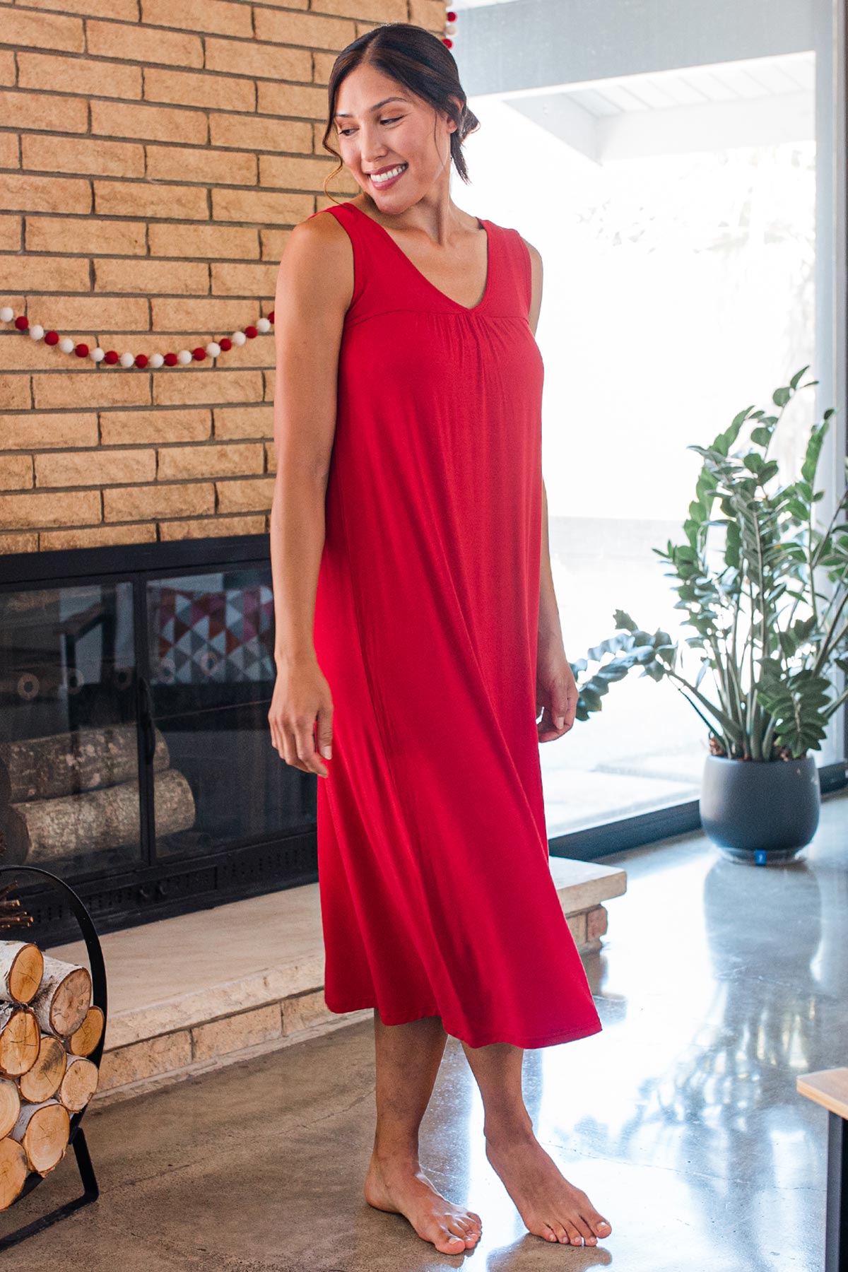 A woman standing and smiling over her shoulder, wearing Yala Molly Sleeveless Bamboo Nightgown in Crimson