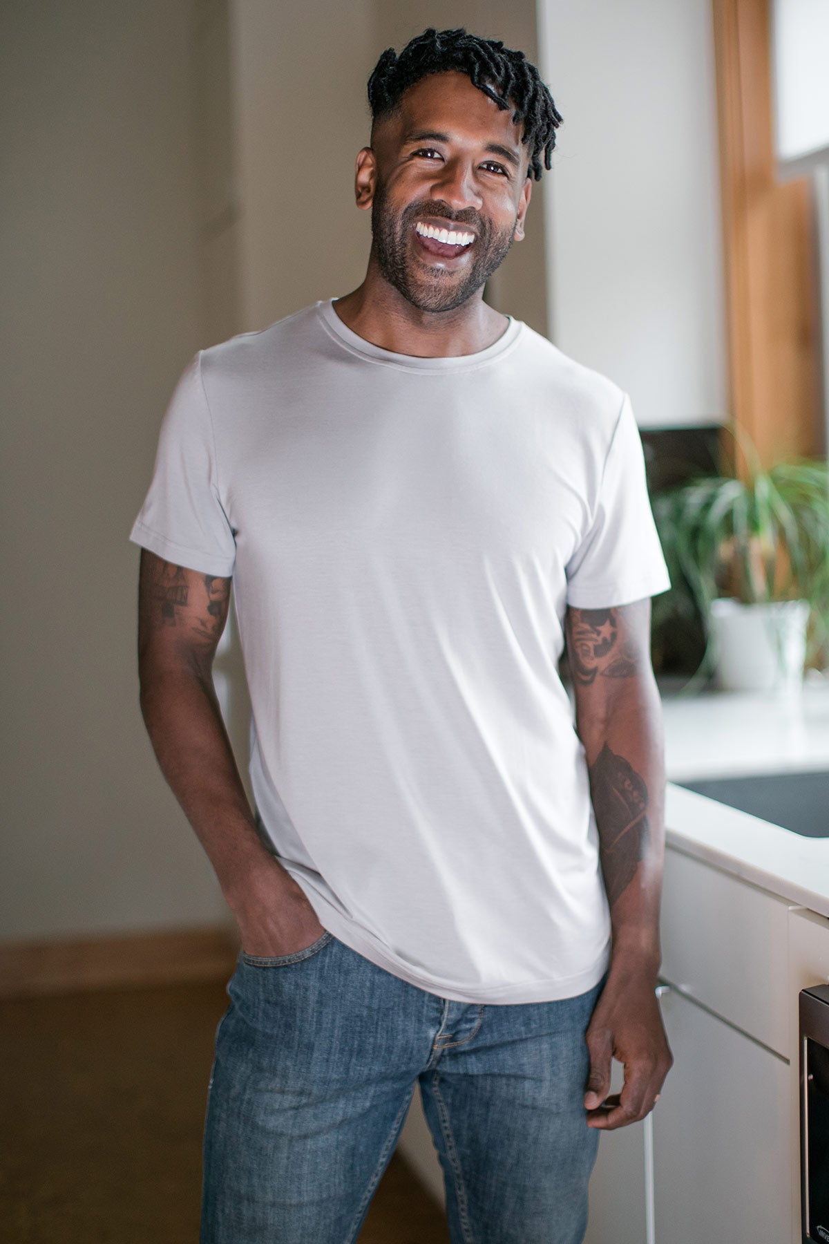 A man standing and laughing with one hand in his pocket, wearing Yala Nathan Men's Short Sleeve Bamboo Crew Tee Shirt in Ash