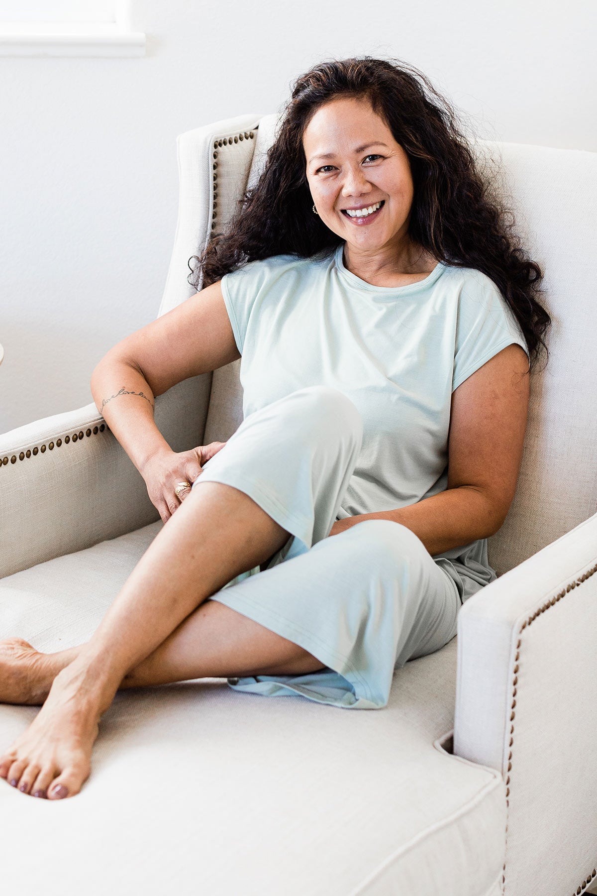 A woman sitting on a chair with her legs crossed and smiling, wearing Yala Opal Swing Lounge Bamboo Pajama Set in Honeydew