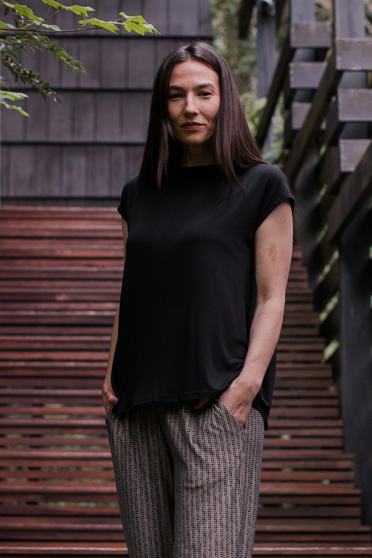A woman standing with both hands in her pockets, wearing Yala Opal Swing Bamboo Top in Black