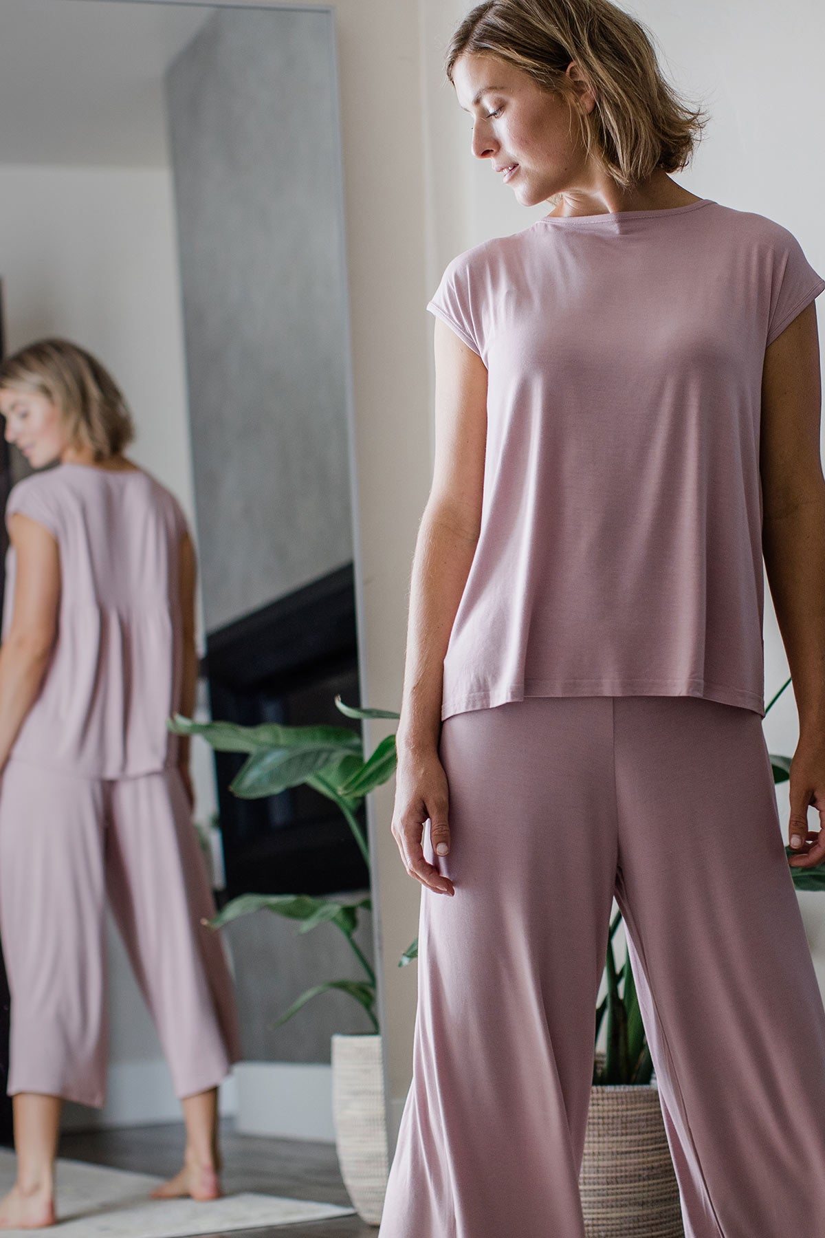 A woman standing and looking back over her shoulder, wearing Yala Opal Swing Lounge Bamboo Pajama Set in Lotus Pink