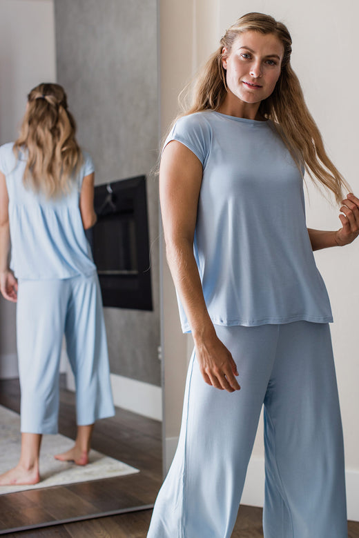 A woman standing with one hand playing with her hair, wearing Yala Opal Swing Lounge Bamboo Pajama Set in Sky