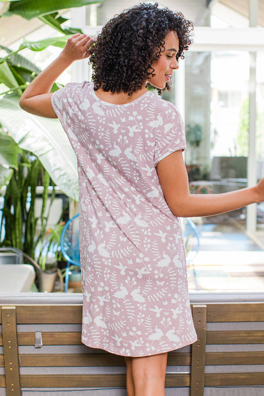 A woman standing facing away from the camera, gazing to the side, wearing Yala Penelope Cap Sleeve Oversized Bamboo Nightshirt in Secret Garden