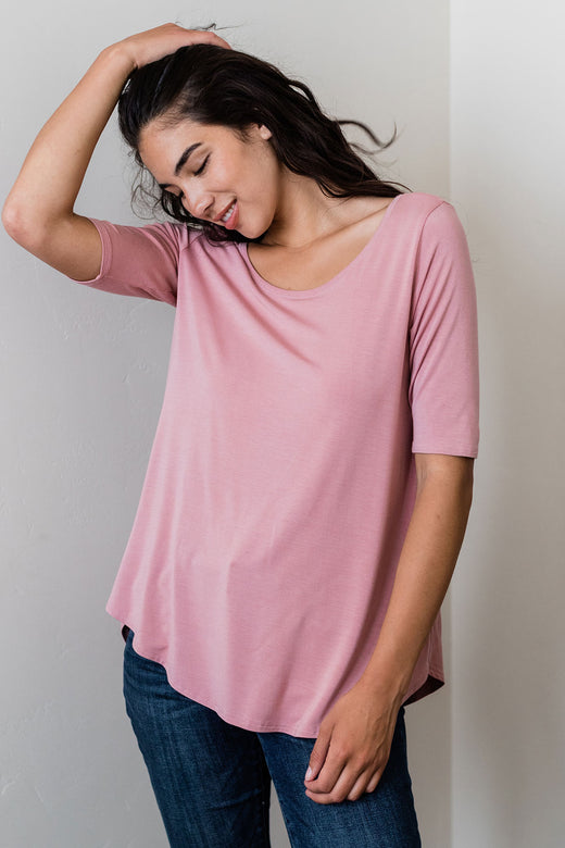 A woman standing and running one hand through her hair, wearing Yala Sandy Relaxed Fit Scoop Neck Short Sleeve Bamboo Top in Cameo