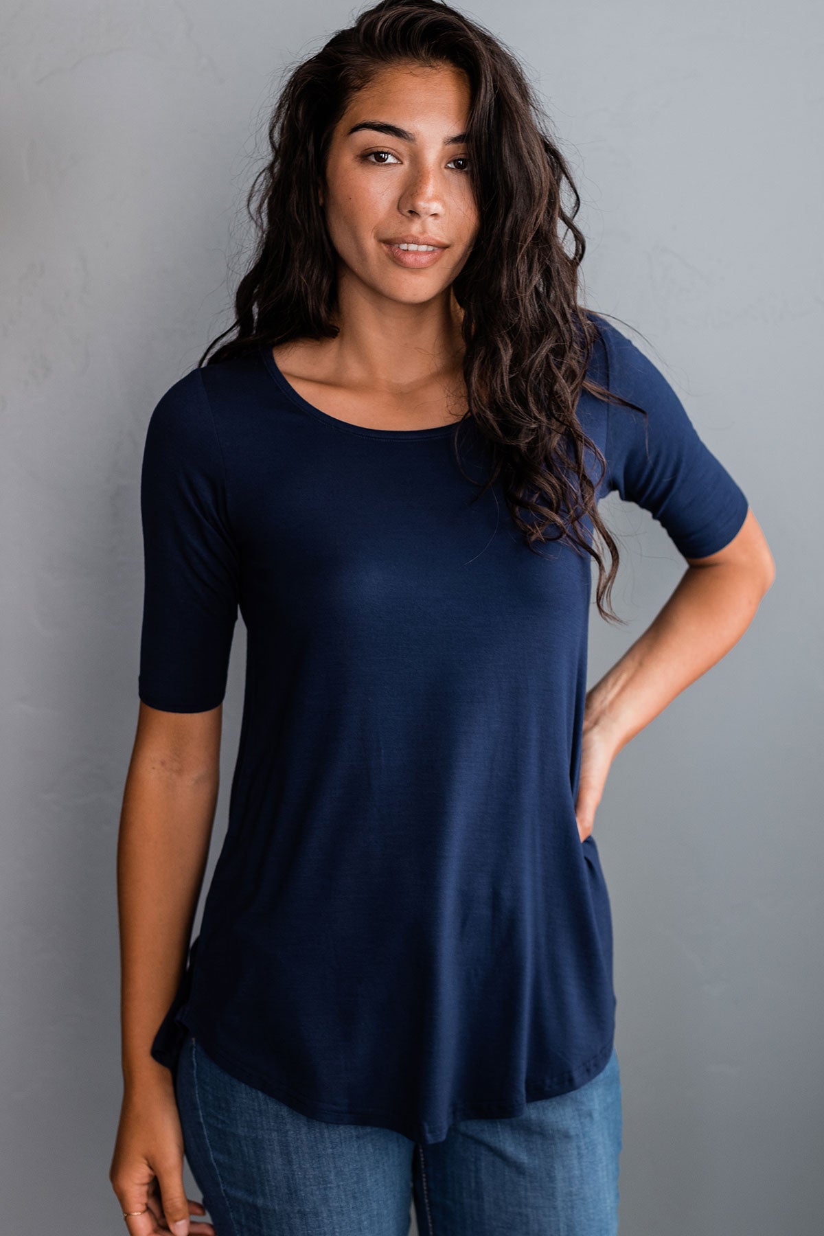A woman standing with one hand on her hip, wearing Yala Sandy Relaxed Fit Scoop Neck Short Sleeve Bamboo Top in Navy