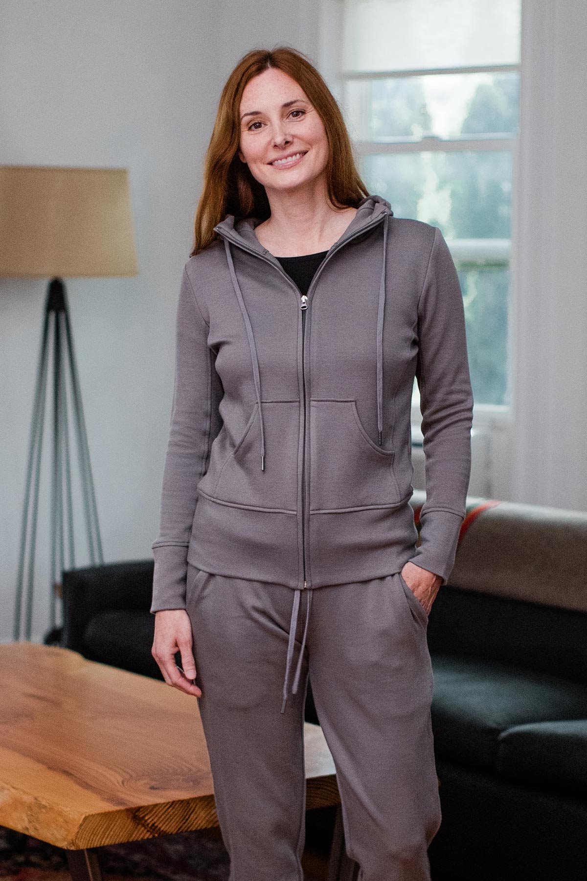 A woman standing and smiling with one hand in her pocket, wearing Yala Scarlet Zip-Up Bamboo and Organic Cotton Hooded Jacket Sweatshirt in Space Grey