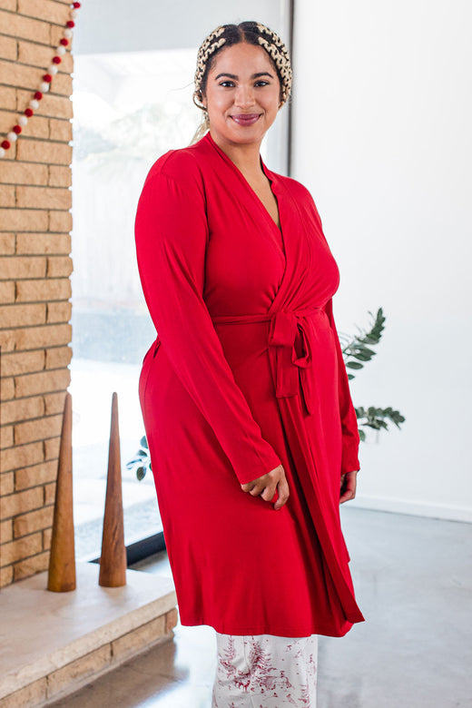 A woman standing facing sideways and looking towards the camera, wearing Yala Serenity Long Sleeve Short Belted Bamboo Robe in Crimson