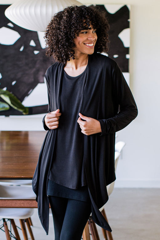 A woman standing and smiling while looking to the side, wearing Yala Sophie Bamboo Cardigan Wrap in Black