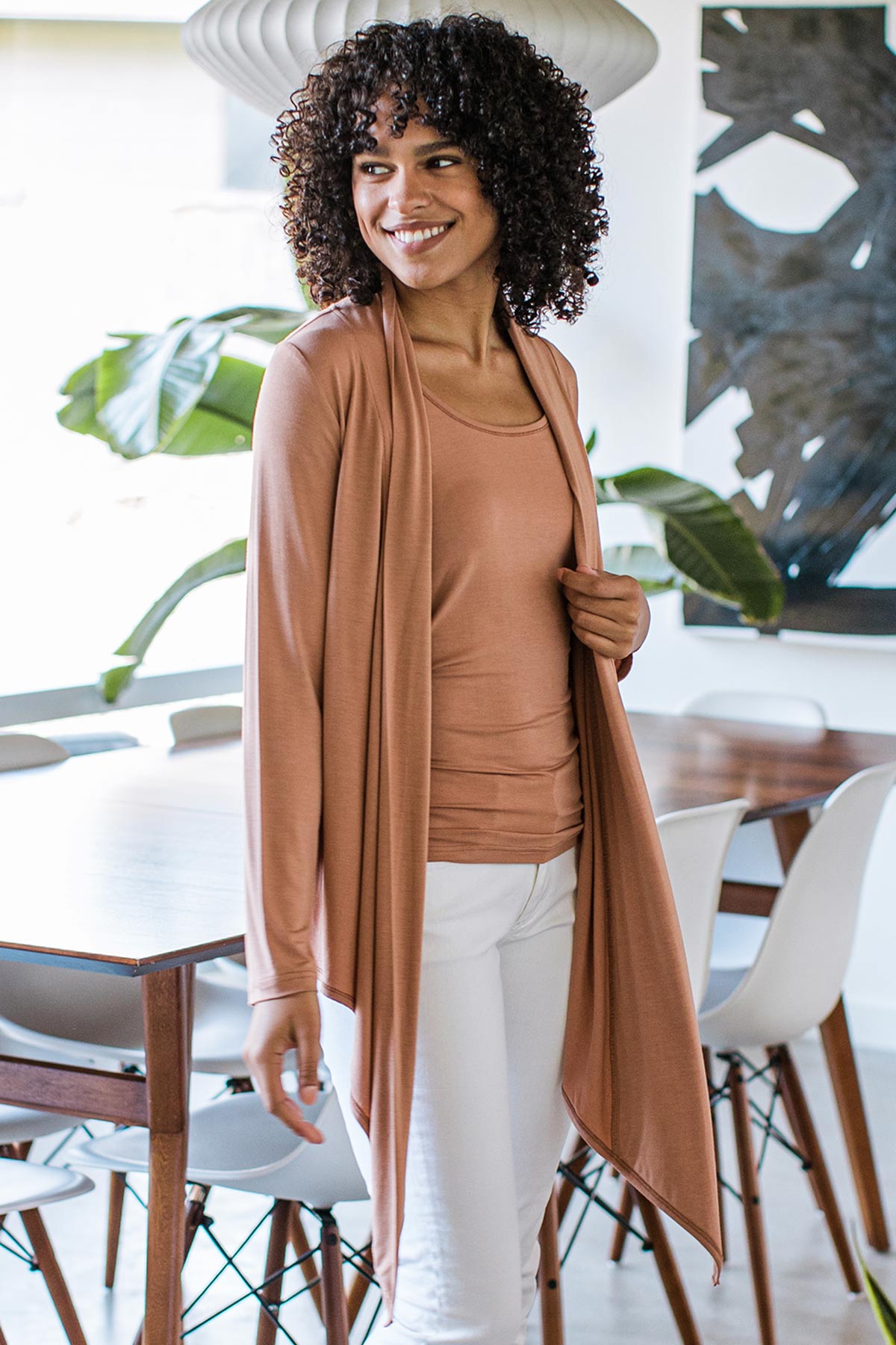 A woman standing somewhat to the side and looking back over her shoulder, wearing Yala Sophie Bamboo Cardigan Wrap in Camel