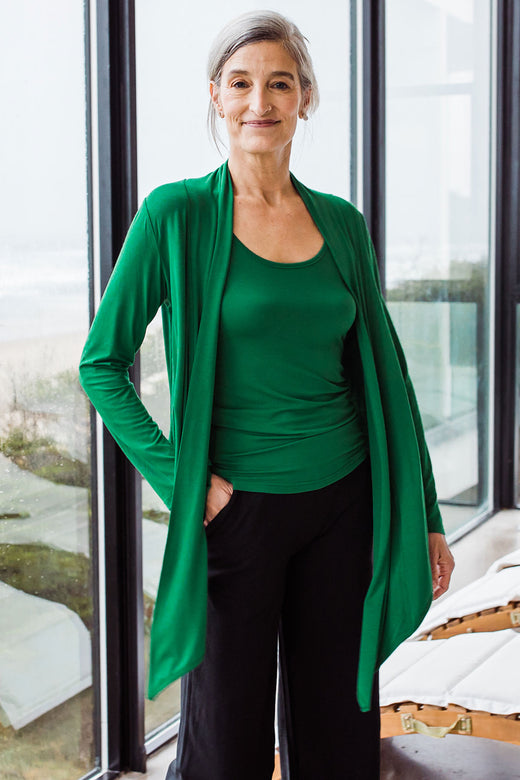 Woman standing in front of a window with one hand in her pocket, wearing Yala Sophie Bamboo Cardigan Wrap in Emerald