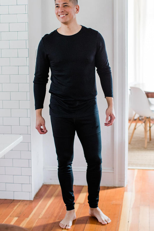 A man standing and smiling while looking slightly to the side, wearing Yala Superfine Merino Wool Leggings in Black
