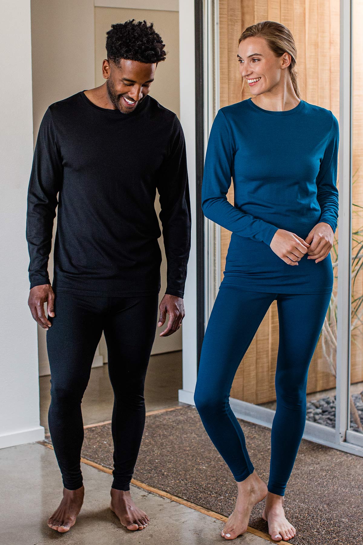 A man and womand stand together smiling, both wearing Yala Superfine Merino Wool Long Sleeve Top in Black and Lapis