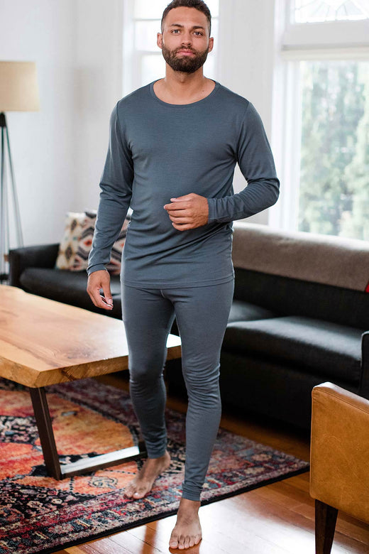 A man standing and striding forward, wearing Yala Superfine Merino Wool Long Sleeve Top and Yala Superfine Merino Wool Leggings in Storm Grey
