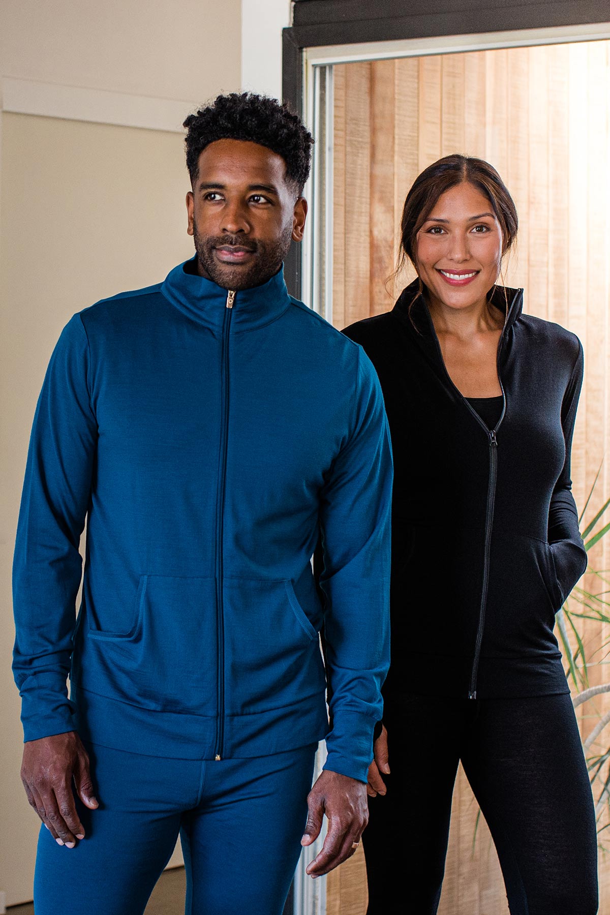 A woman and man standing together, smiling and both wearing Yala Superfine Merino Wool Track Jacket in Black and Lapis