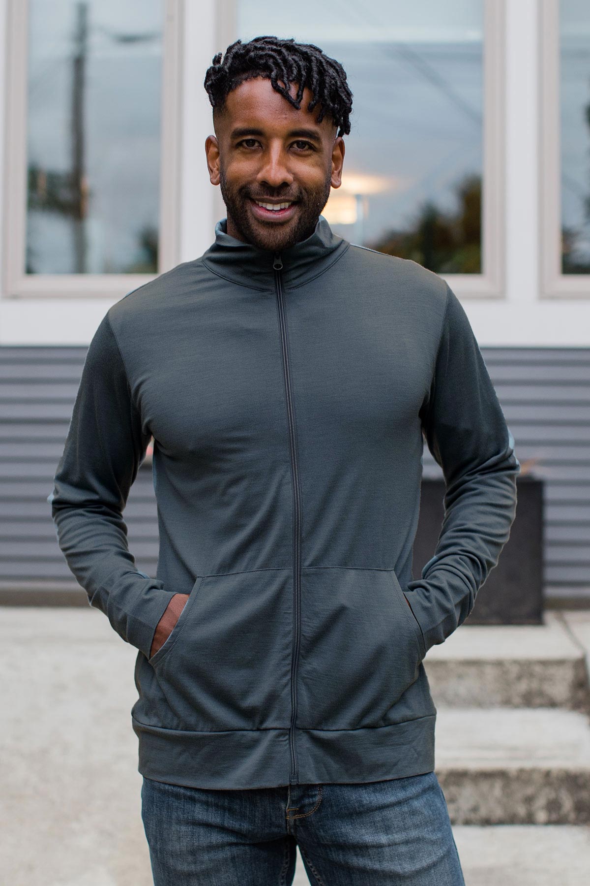A man standing and smiling with both hands in his jacket pockets, wearing Yala Superfine Merino Wool Track Jacket in Storm Grey