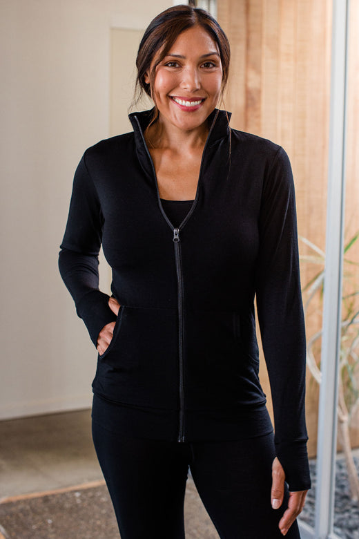 A woman standing and smiling, one hand in her jacket pocket, wearing Yala Superfine Merino Wool Track Jacket in Black