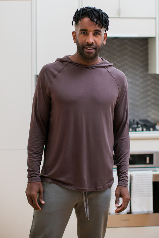 A man standing with his hands at his sides, wearing Yala Travis Men's Hooded Long Sleeve Raglan Bamboo Tee Shirt in Mink