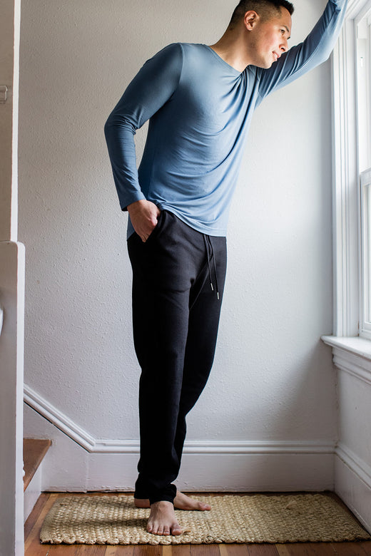 A man standing and leaning forward against a window with one hand in his pocket, wearing Yala Zach Men's Bamboo and Organic Cotton Sweatshirt Jogger Lounge Pants in Black