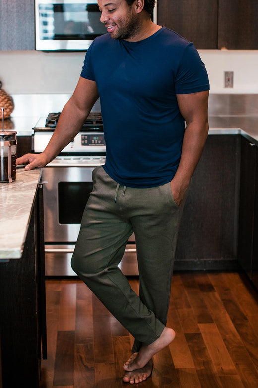 A man standing at a countertop with one knee bent, wearing Yala Zach Men's Bamboo and Organic Cotton Sweatshirt Jogger Lounge Pants in Moss
