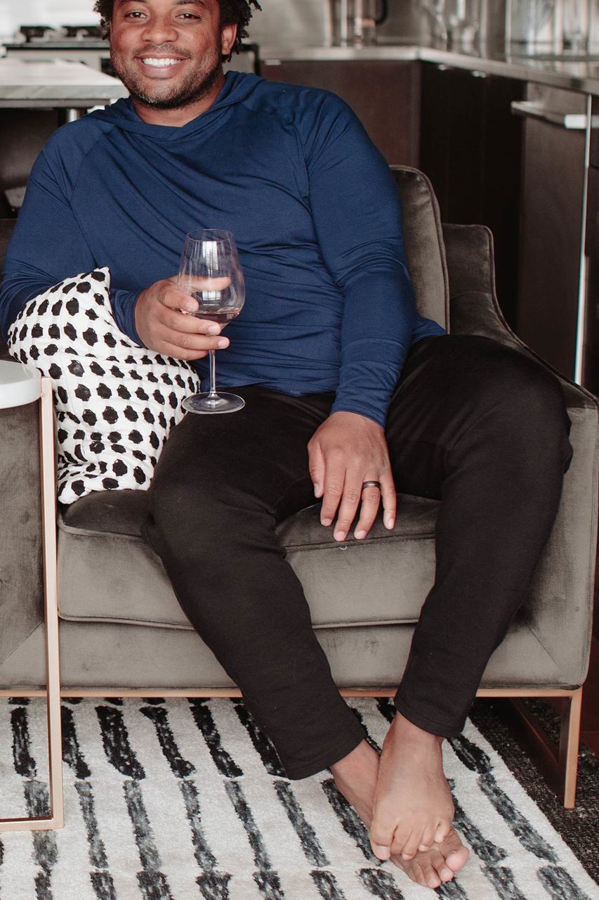 A man sitting in a chair and smiling while holding a glass of wine and leaning to the side, wearing Yala Zach Men's Bamboo and Organic Cotton Sweatshirt Jogger Lounge Pants in Black