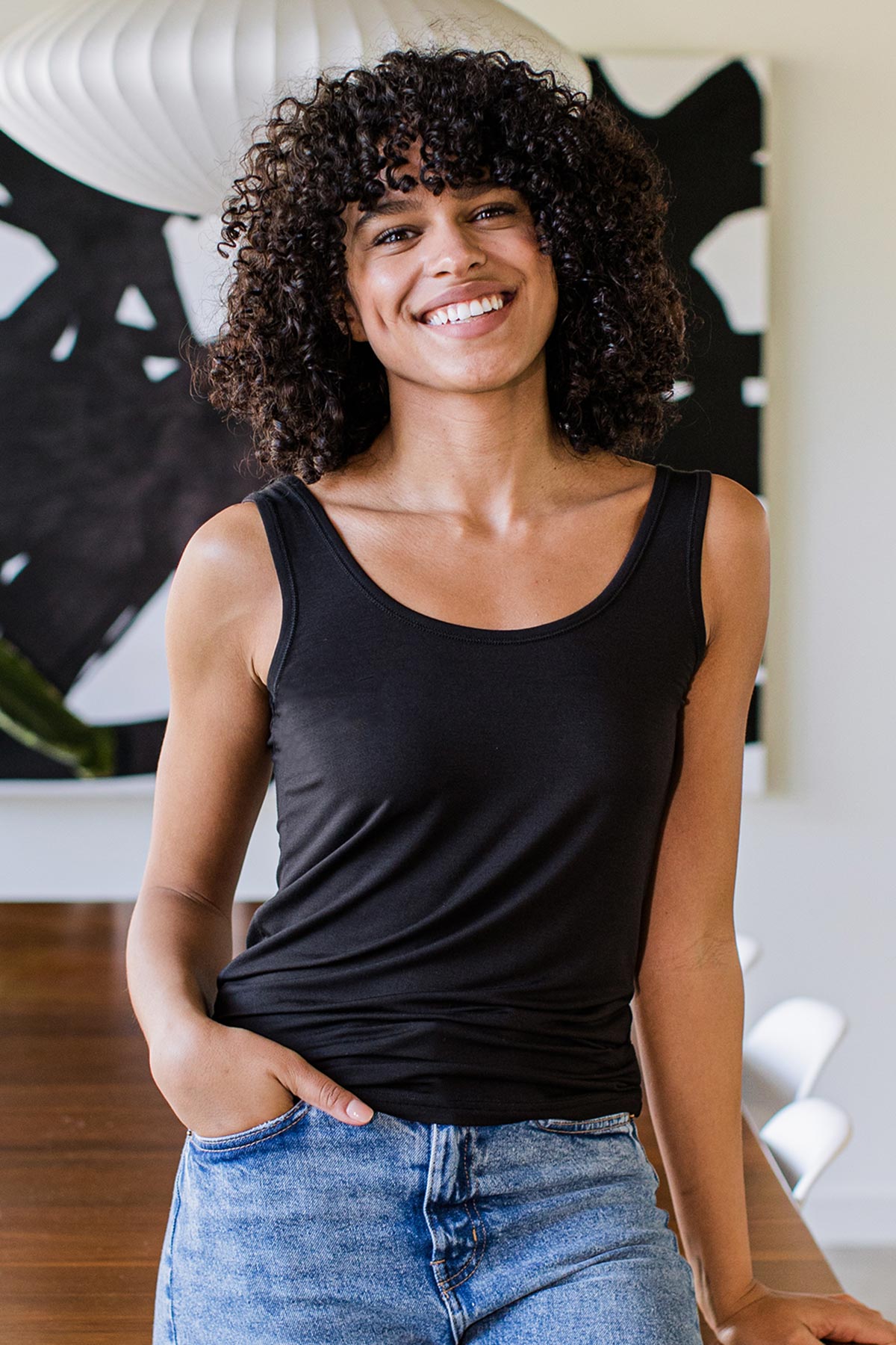 A woman standing and smiling with one hand in her pocket, wearing Yala Zia Layering Bamboo Tank Top in Black