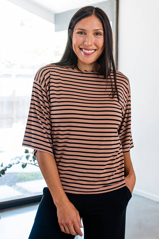 A woman standing and smiling with one hand in her pocket, wearing Yala Jaclyn Wide Sleeve Boatneck Bamboo Top in Black Newport Stripe
