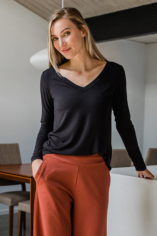 A woman standing with one hand in her pocket, wearing Yala Jill V-Neck Long Sleeved Bamboo Top in Black