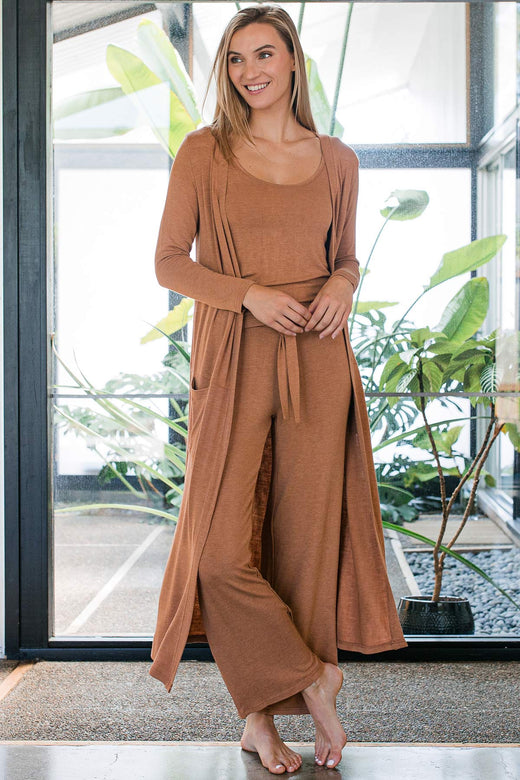 A woman standing with one leg crossed in front of the other, wearing Yala Peyton Bamboo Sweater Drawstring Bamboo Lounge Pants in Camel