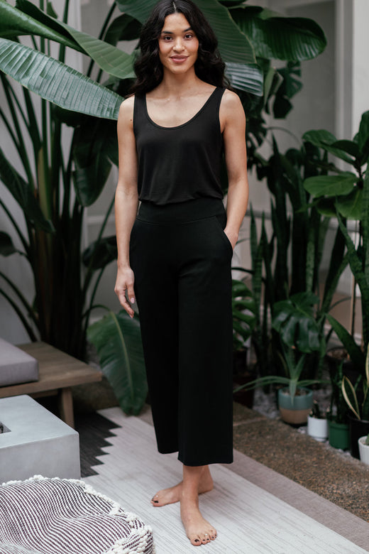A woman standing with one hand in her pocket, wearing Yala Billie Ultra-Stretch Bamboo and Organic Cotton Classic Wide Leg Cropped Pants in Black