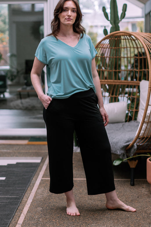 A woman standing with one leg extended to the side and one hand in her pocket, wearing Yala Billie Ultra-stretch Bamboo and Organic Cotton Classic Wide Leg Cropped Pants in Black