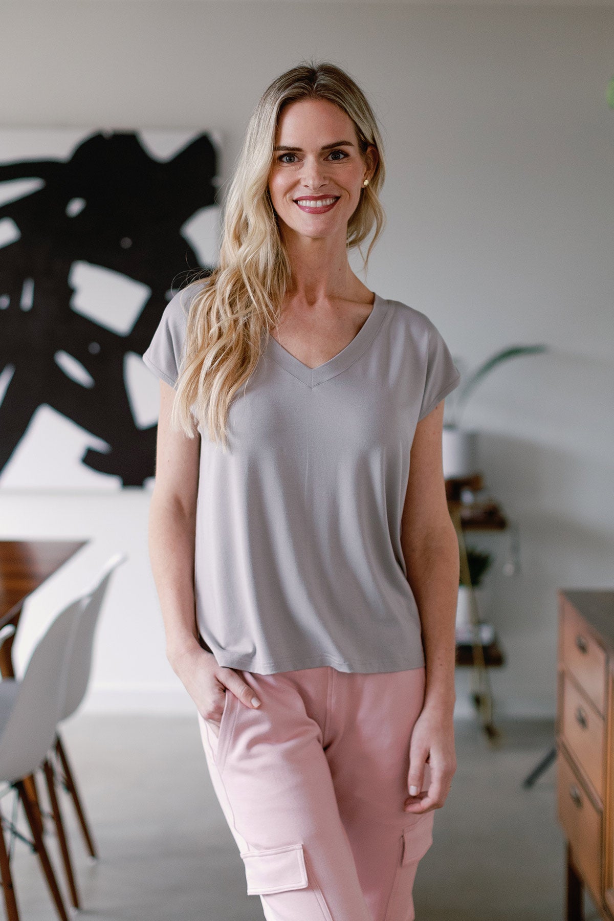 A woan standing and smiling with one hand in her pocket, wearing Yala Dakota V-Neck Cap Sleeve Bamboo Top in Ash