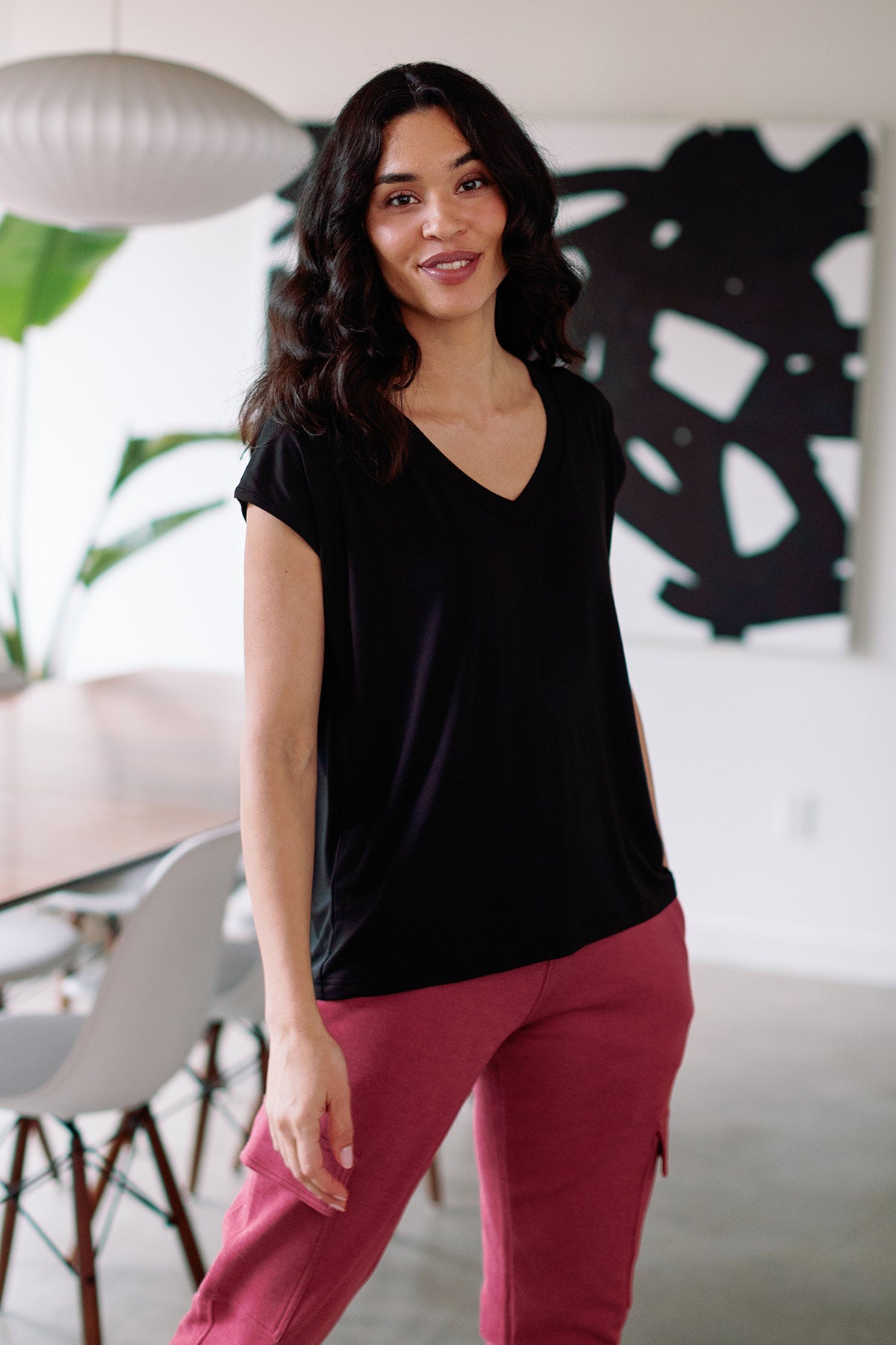 A woman standing with one leg extended to the side, wearing Yala Dakota V-Neck Cap Sleeve Bamboo Top in Black