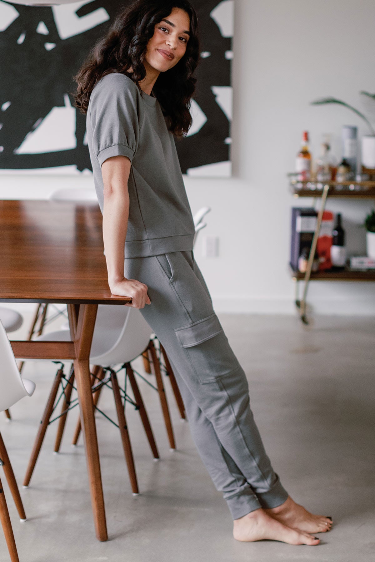 A woman leaning again the top of a table, wearing Yala Fay Bamboo and Organic Cotton Cargo Joggers in Space Grey