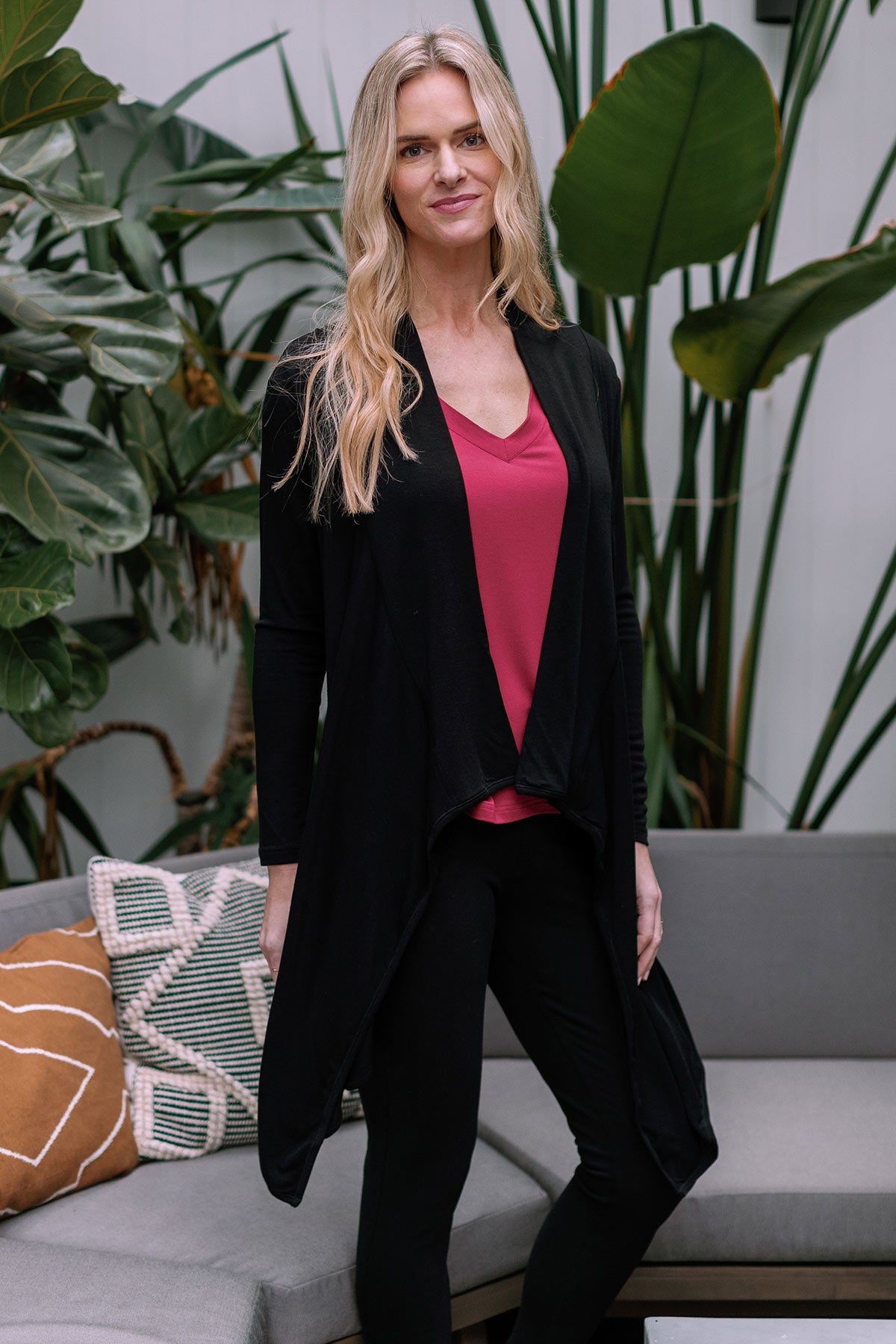 A woman standing with one knee bent to the side, wearing Yala Hilary Bamboo Sweater Wrap in Black